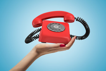 Side closeup of woman's hand facing up and holding ringing retro phone on light blue background.
