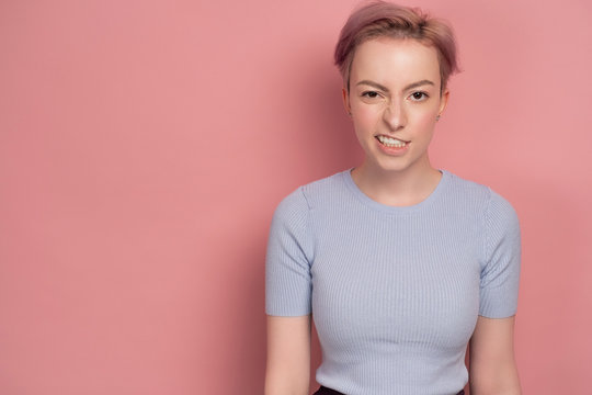 Pink-haired young woman makes a funny face expression, pink background