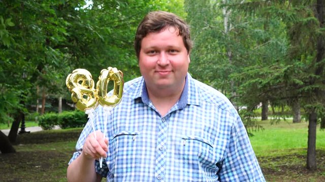 Big man holding golden balloons making the 80 number outdoor. 80th anniversary celebration party