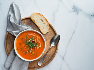 Gaspacho soup on round wooden tray over white marble tabletop. Bowl of traditional spanish cold soup puree gazpacho on light marble background. Copy space for text or design. Top view or flat lay.
