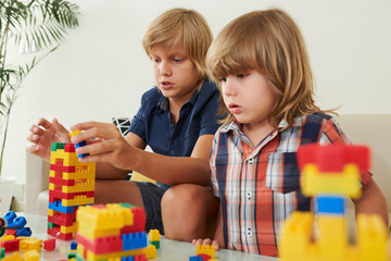 Amazed little boy looking at his older brother making cool high tower out of colorful plastic blocks