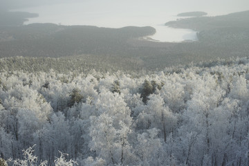 View from the top of the mountain to the forest covered with hoarfrost and a frozen mountain lake on a frosty sunny day. High resolution and detail.