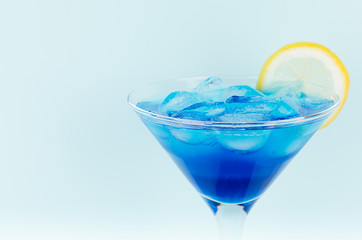 Refreshing alcohol drink blue Hawaii in misted rich wine glass with ice cubes, lemon slice in modern pastel mint background, closeup, head, details.