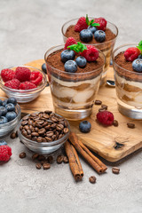 Classic tiramisu dessert with blueberries and raspberries in a glass on concrete background
