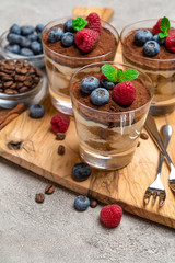 Classic tiramisu dessert with blueberries and raspberries in a glass on concrete background