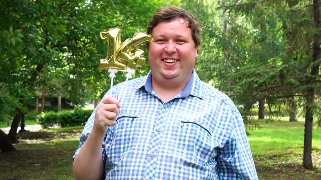 Big man holding golden balloons making the 14 number outdoor. 14th anniversary celebration party