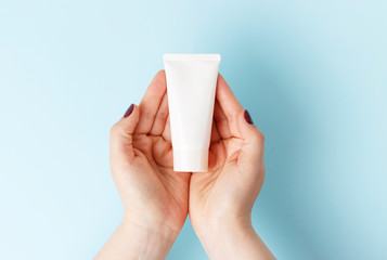Tube with cream in female hands, blue background, top view, cosmetics care concept