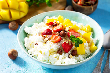 Dietary breakfast for summer time. Fresh cottage cheese with strawberry, mango and nuts on a light blue stone or slate table.