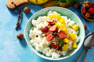 Dietary breakfast for summer time. Fresh cottage cheese with strawberry, mango and nuts on a light blue stone or slate table.  Free space for your text.