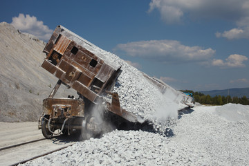 Unloading of gravel from the railway dump-car, closeup. Mining industry. Quarry and mining equipment.