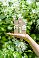 The girl holds the house symbol against the background of blossoming appletree 