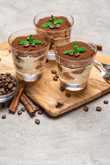 Classic tiramisu dessert in a glass cup on wooden cutting board on concrete background