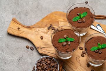 Classic tiramisu dessert in a glass cup on wooden cutting board on concrete background