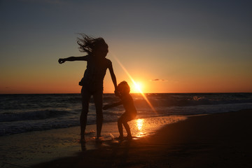 Silhouette of mother and son playing on the beach at the sunset.  Concept of family life and joy,...