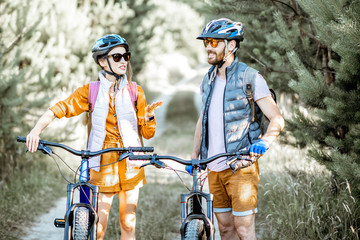 Young couple dressed casually talking together while traveling with mountain bicycles on the forest...