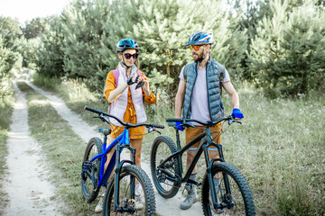 Young couple dressed casually talking together while traveling with mountain bicycles on the forest road