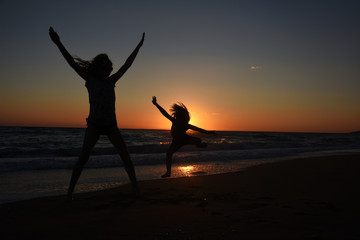 Silhouette of mother and son playing on the beach at the sunset.  Concept of family life and joy, summer vacations