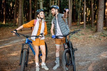 Obraz premium Young couple dressed casually standing together with mountain bicycles, traveling in the forest during the summer vacations