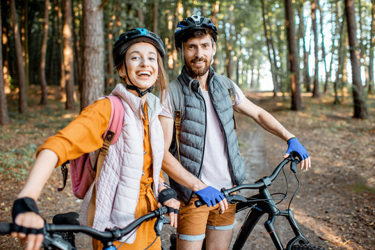 Portrait of a young couple dressed casually standing together with mountain bicycles, traveling in the forest during the summer vacations