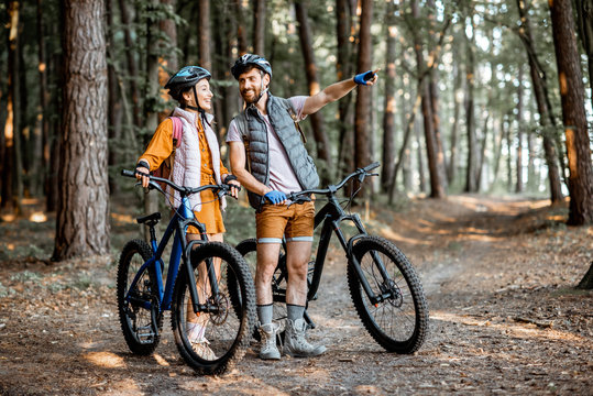 Young couple dressed casually standing together with mountain bicycles, traveling in the forest during the summer vacations