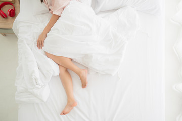 Fototapeta na wymiar Beautiful crossed woman legs relaxing lying on bed with white duvet in bedroom, top view, copy space