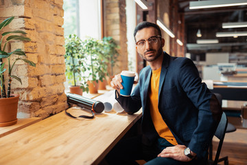 Handsome bearded man drinking coffee sitting near window