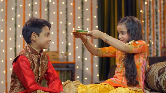 Smiling and cute young Indian siblings celebrating Raksha Bandhan / Bhai Dooj traditions - festival concept . Cute little sister doing aarti / pooja of her brother on the occasion of Raksha Bandhan