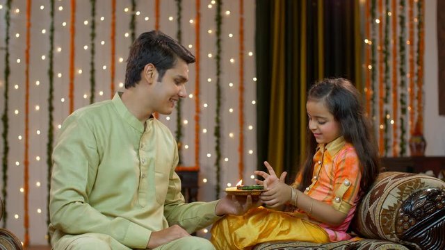 Young siblings celebrating Raskha Bandhan / Bhai Dooj festival together - Happy family. Pretty sister happily putting tika on her elder brother's forehead in traditional wear on the occasion 