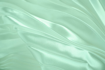 Neo mint color soft satin folded fabric background texture. Close up of ripples on silk fabric. Neo...