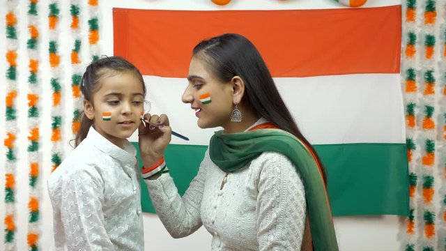 Indian woman painting the face of a little girl in Tricolors of a national flag - Independence Day / Republic Day concept. Beautiful woman paints the cheeks of a cute girl. Draw a flag - Celebration