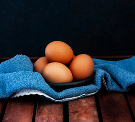 EGGS ON BLACK BOWL AND BLUE FABRIC CLOTH ON RUSTIC WOODEN TABLE