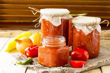 Homemade preserving. Tomato sauce with vegetables on the kitchen wooden background. Copy spase.