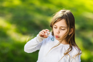 young girl blowing soap bubbles in park