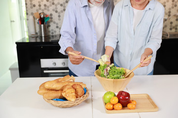close up caucasian elderly wife making salad in the kitchen with her elderly husband happily during his retirement life on table with fruits in happy holiday