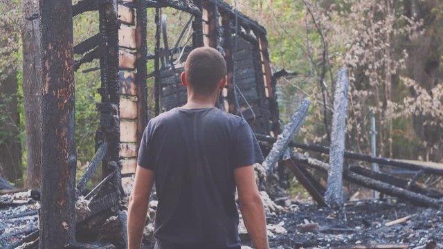 Portrait of a sad man on the background of a burned house, after fire . Consequences of fire disaster accident. Ruins after fire disaster, despair concept.