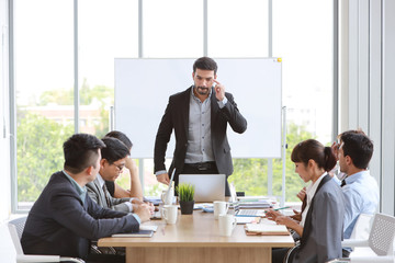 caucasian lecturer giving public presentation with company business graph result on white board in meeting room and multiethnic business people are paying attention (training or seminar concept)