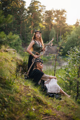 Two beautiful, forest witches stand on a hill with a staff next to the forest. Druids. Fantasy image