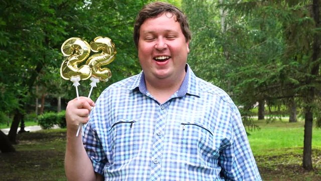 Big man holding golden balloons making the 22 number outdoor. 22th anniversary celebration party