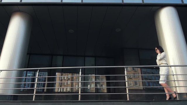 Woman walking and talking on cellphone in the city near scyscraper building in slow motion.
