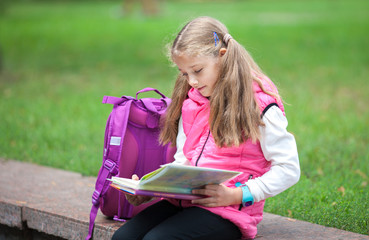 Schoolgirl with a backpack and book outdoors. Education and learning concept.