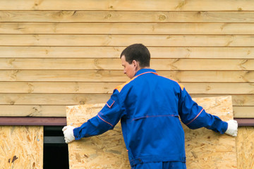 a man in a blue jumpsuit closes the bottom of the house with a wooden shield