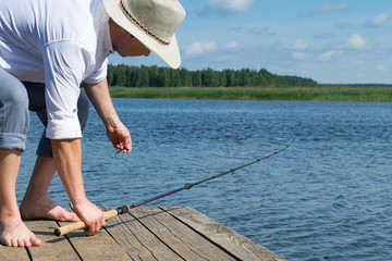 a man in a hat takes a fishing rod on the background of a beautiful morning lake