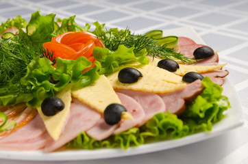banquet cutting with ham, meat delicacies, cheese, sausage smoked, olive, lettuce and tomato on white dish