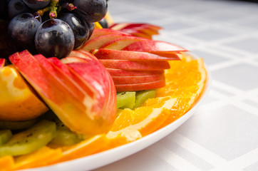 sliced fruit - apples, oranges, kiwi topped with grapes on white dish