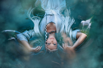 A girl elf in a white dress is floating in the water. Model in a medieval dress with pigtails...