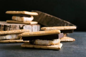 Delicious s`mores with pieces of chocolote and roasted marshmallow on the grey rustic surface