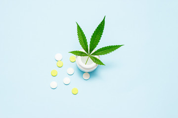 Fototapeta na wymiar Marijuana leaf in medical pills bottle on blue background. The concept of legalization of marijuana.