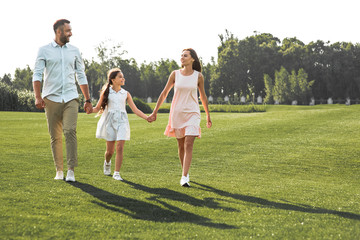 Enjoying time together. Full length of happy and young family of three holding hands, smiling and...