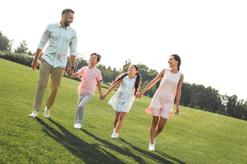 We are happy together Full length of positive and young family of four holding hands, smiling and...