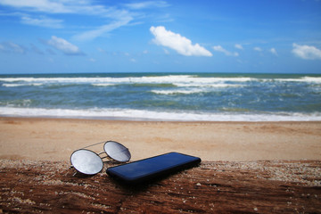 Fototapeta na wymiar Sunglasses and phone are placed on dry logs and reflections of bright sky
